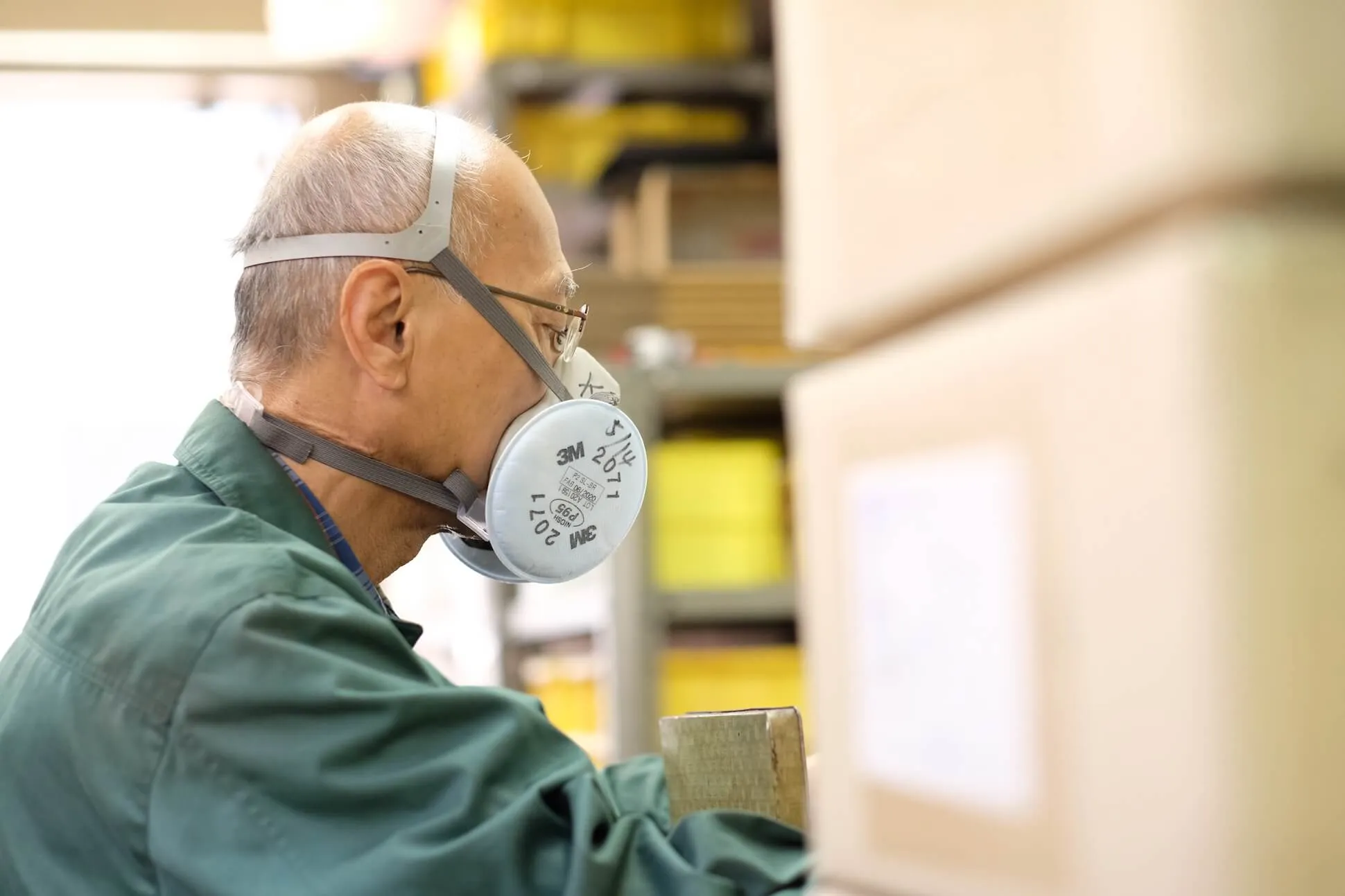 Close view of a Nonaka craftsman at work beside shelves of workshop materials